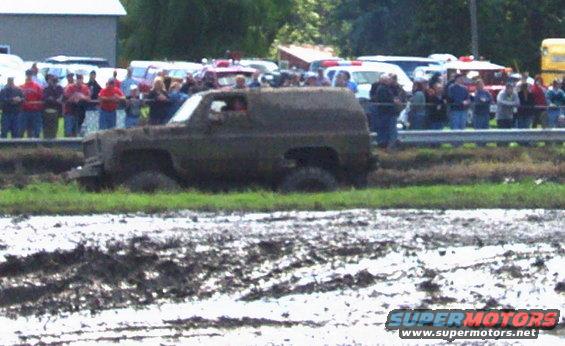Mud-covered SUV stuck in mud with spectators in the background