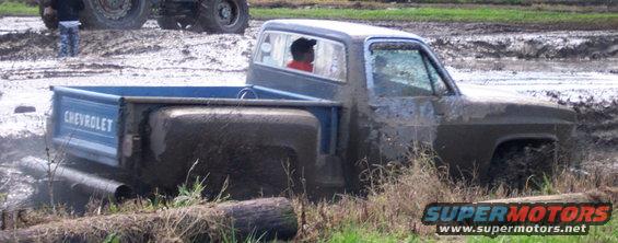 Blue Chevrolet pickup truck stuck in mud with a person inside