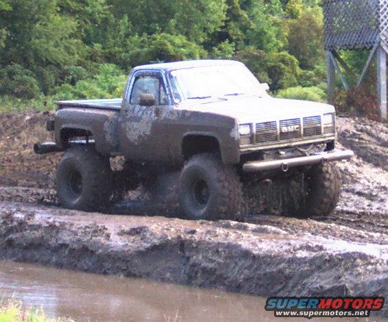 Mud-splattered GMC pickup truck with large tires driving through mud