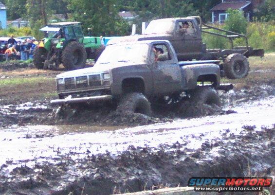 Mud bogging trucks stuck in mud, one with a roll cage