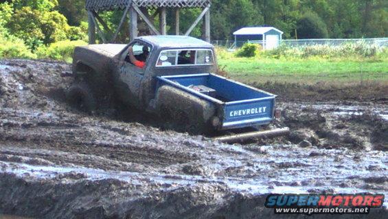 Chevrolet pickup truck with blue bed stuck in mud, driver visible