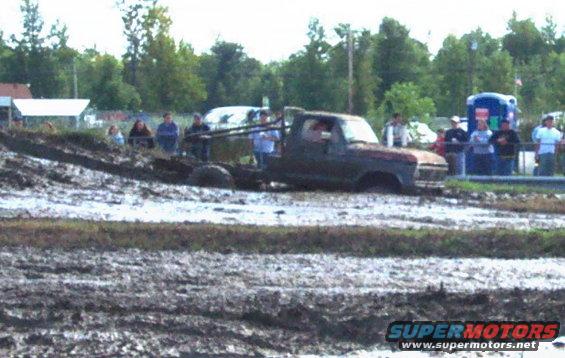 Truck stuck in mud pit with people watching