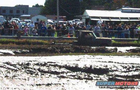 Mud-splattered truck driving through a mud pit with spectators watching
