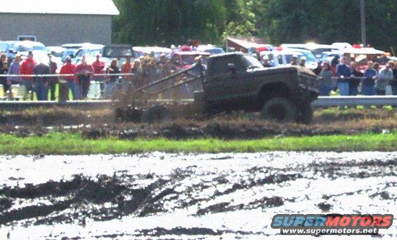 Modified pickup truck participating in a mud bog event with spectators in the background