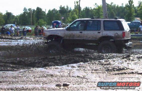 SUV stuck in mud pit, people watching in background