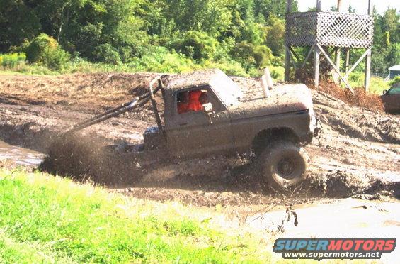 Mud-covered 1979 Ford Bronco navigating a muddy track with large tires and roll cage