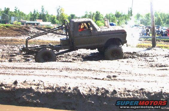 Mud-covered truck with roll cage and exhaust stack in a mud pit