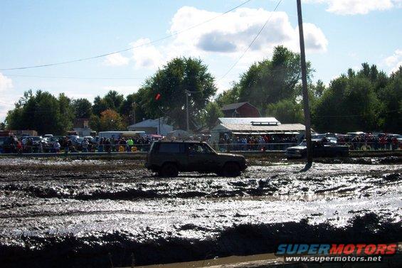 Dark colored SUV driving through a muddy track with spectators in the background