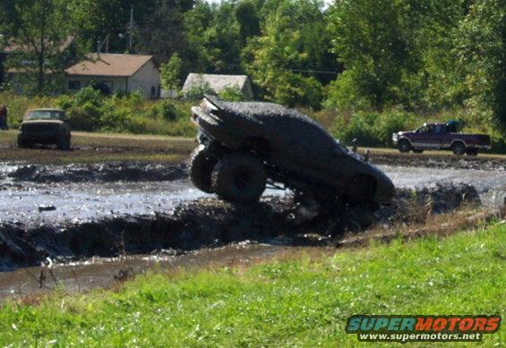 Muddy SUV stuck in a mud pit, tires high in the air