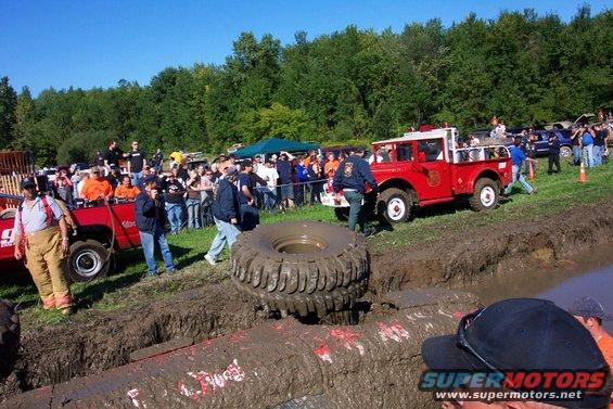 Mud bogging event with a red fire truck and other vehicles, spectators watch from the side