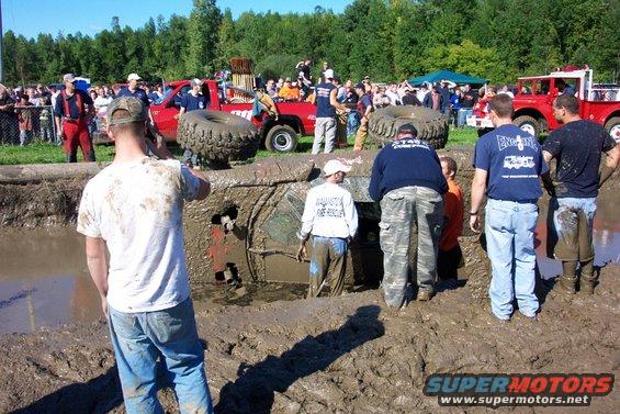 Mud bog event with a vehicle stuck deep in the muck and spectators around