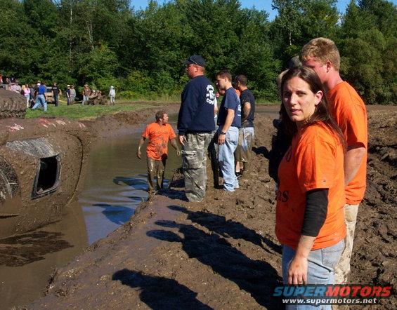 Mud-covered vehicle stuck in a mud pit with onlookers