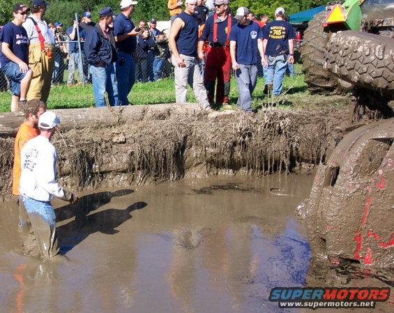 Mud-covered vehicle part in muddy water with people watching