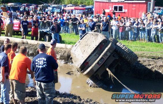 Mud-covered SUV stuck at an angle in a mud pit, with spectators watching