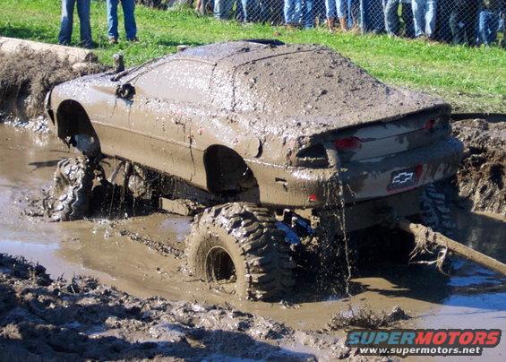 Mud-covered car stuck in a mud pit with large off-road tires