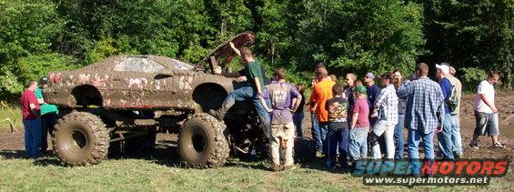 Mud-covered lifted truck with large tires, people gathered around watching
