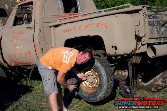Guy working on a muddy pickup truck with names written on the side and 'Happy B-Day Doug' on the fender