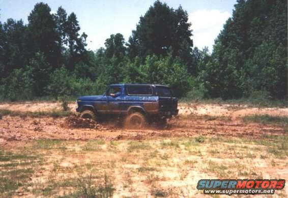 Blue Ford Bronco stuck in mud, driving off-road. Model appears to be from the late 1970s