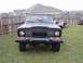 1977 Jeep Wagoneer - Front view of a black 1977 Jeep Wagoneer parked on grass with a trailer behind it.