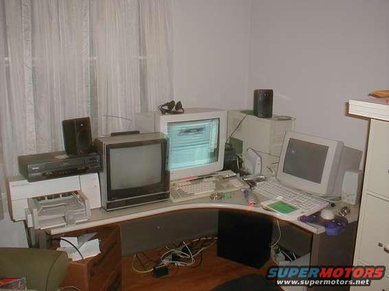 Computer desk with multiple monitors, keyboards, speakers, and a printer