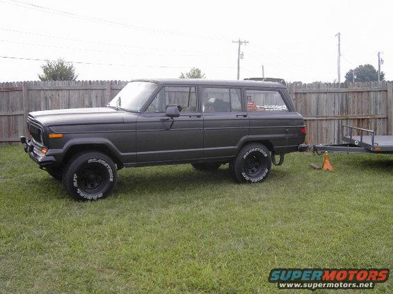 Dark gray Jeep Grand Wagoneer parked on grass, hitched to a trailer