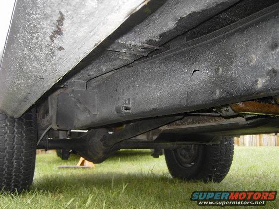 Underside view of vehicle frame, leaf springs, and rear axle. Tires visible