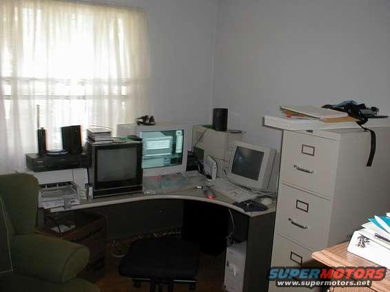 office desk with multiple computer monitors, keyboards, and a filing cabinet