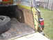 1977 Jeep Wagoneer - The rear cargo area of a yellow 1977 Jeep Wagoneer shows a spare tire and a worn floor, with visible text on the rear window.