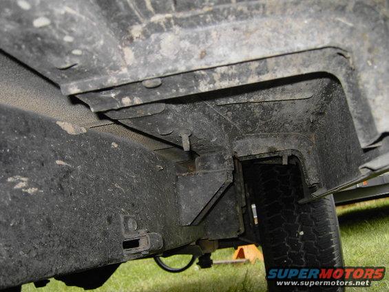 Close-up of vehicle frame and tire, showing suspension components and undercarriage. Supermotors.net logo visible