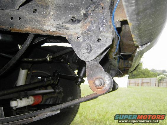 Underside of a vehicle showing suspension components, leaf spring, and frame. Some rust is visible