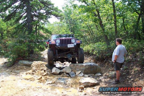Jeep Wrangler TJ going over rocks on a trail. Guy watches from the side