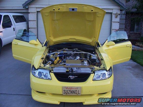 Yellow 2002 Ford Mustang, front view, hood and driver's side doors open, showing engine bay. California license plate reads SUZNNOL