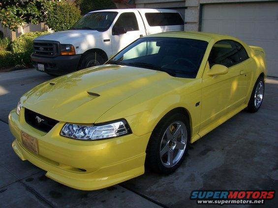 Yellow 2002 Ford Mustang coupe parked in driveway next to a white Ford truck