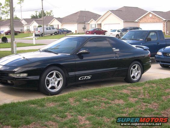 Black coupe with white racing stripes and 'GTS' decal on the side. Other vehicles visible in background