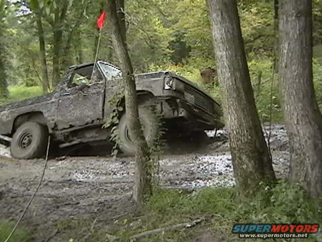 Mud-covered truck stuck in a wooded area, front grille visible
