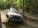 1988 Ford Bronco - A pickup truck navigates a challenging, muddy off-road path through a wooded area.