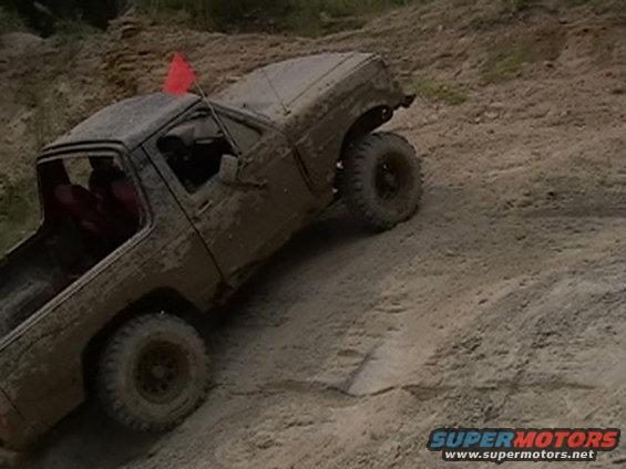 Mud-covered truck with red flag on roof, driving on dirt hill