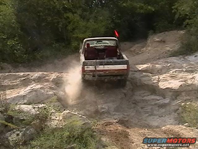 Pickup truck driving up a dusty, rocky incline with trees in the background