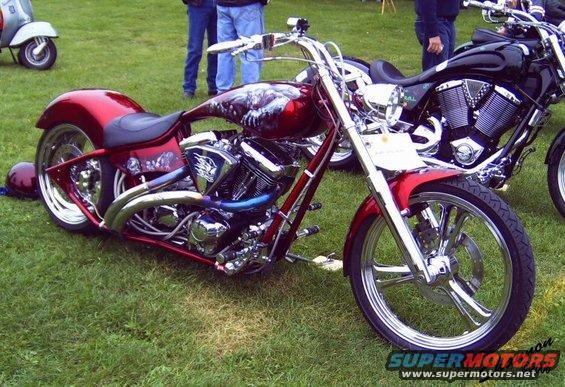 Red custom motorcycle with chrome accents and skull graphics on the fuel tank, parked on grass