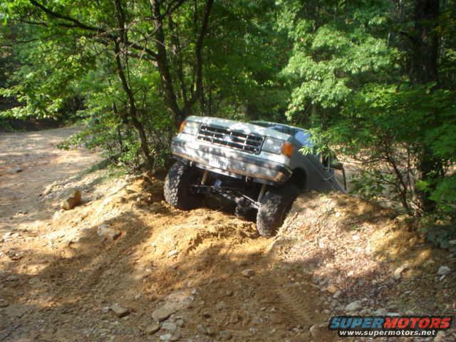 White 1987 Ford Bronco climbing a dirt hill, front 3/4 view, off-road tires