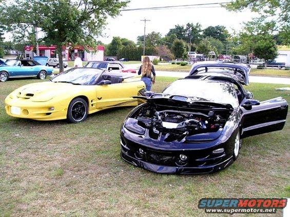 Black 1998 Pontiac Firebird with hood and doors open, parked next to a yellow convertible Firebird