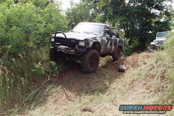 Camouflaged Toyota pickup truck climbing a dirt hill, with a white Jeep in the background