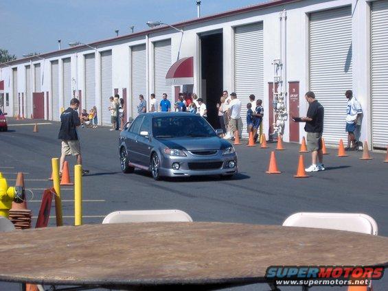 Gray sedan with aftermarket body kit driving on asphalt course with orange cones