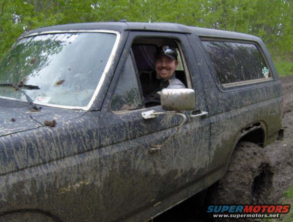 Mud-covered 1989 Ford Bronco with driver, stuck in mud
