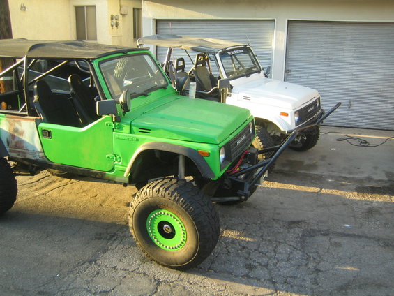 Green 1987 Suzuki Samurai with off-road modifications and a white Suzuki Samurai behind it