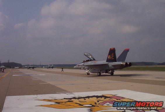 Fighter jet on an airport runway with other aircraft in the background