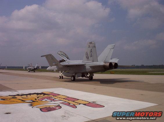Gray fighter jet on tarmac with open canopy and visible markings