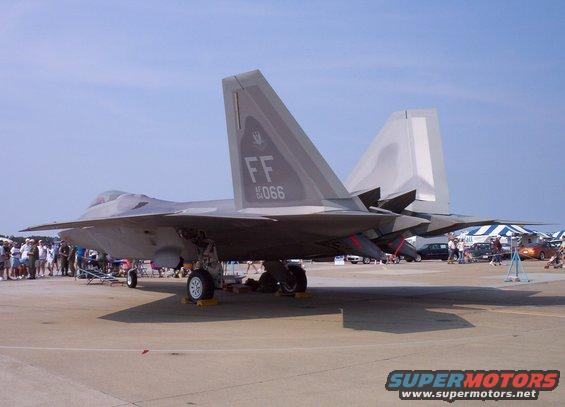 F-22 Raptor fighter jet on tarmac with people and tents in background