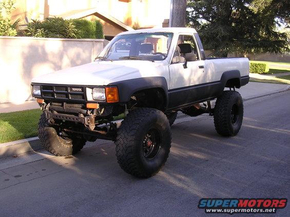 White 1985 Toyota pickup truck with large off-road tires and lifted suspension