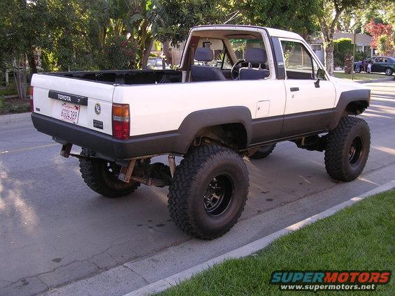 White Toyota pickup truck with lifted suspension and large tires, seen from the rear